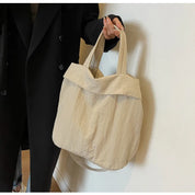 Borsa shopper beige in tessuto, design minimalista, manici lunghi, indossata da persona con cappotto nero. Accessorio moda casual ed elegante.