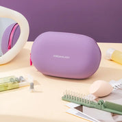 Astuccio cosmetico viola Jordan & Judy su tavolo beige, con specchio, spazzola, spugna trucco e flacone. Accessori bellezza eleganti e funzionali.