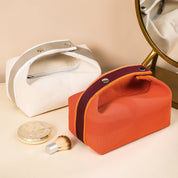 Due beauty case in tessuto, uno arancione e uno bianco, con specchio e cipria. Eleganti e pratici per organizzare cosmetici e accessori.