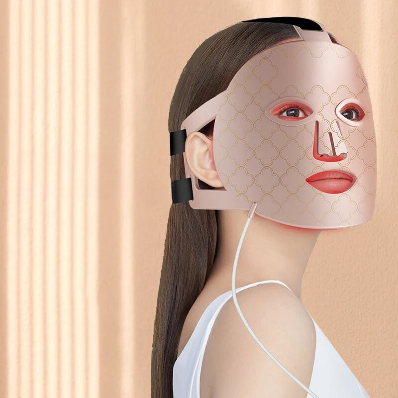 Donna con maschera LED per terapia della pelle, design elegante, colore rosa, utilizzata per trattamenti anti-età e cura del viso, sfondo beige.