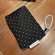 Pochette nera trapuntata con perline bianche, manico a perle, su tavolo in legno. Elegante accessorio moda, ideale per eventi serali.