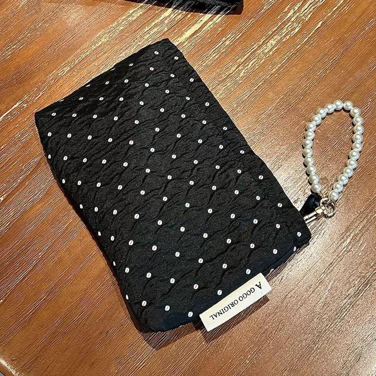 Pochette nera trapuntata con perline bianche, manico a perle, su tavolo in legno. Elegante accessorio moda, ideale per eventi serali.