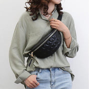 Donna con camicia verde e jeans indossa marsupio nero trapuntato. Accessorio moda casual, borsa a tracolla elegante e pratica.