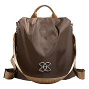 Zaino moda marrone in nylon con manico superiore, tracolla regolabile e decorazione metallica frontale. Accessorio elegante e funzionale per donna.