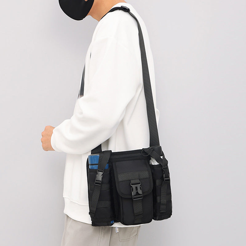 Uomo con felpa bianca indossa borsa a tracolla nera multifunzione, tasche multiple, stile casual urbano. Accessorio moda maschile pratico e trendy.