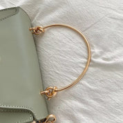 Borsa in pelle verde salvia con manico in metallo dorato su tessuto bianco. Design elegante, accessorio moda donna, stile contemporaneo.