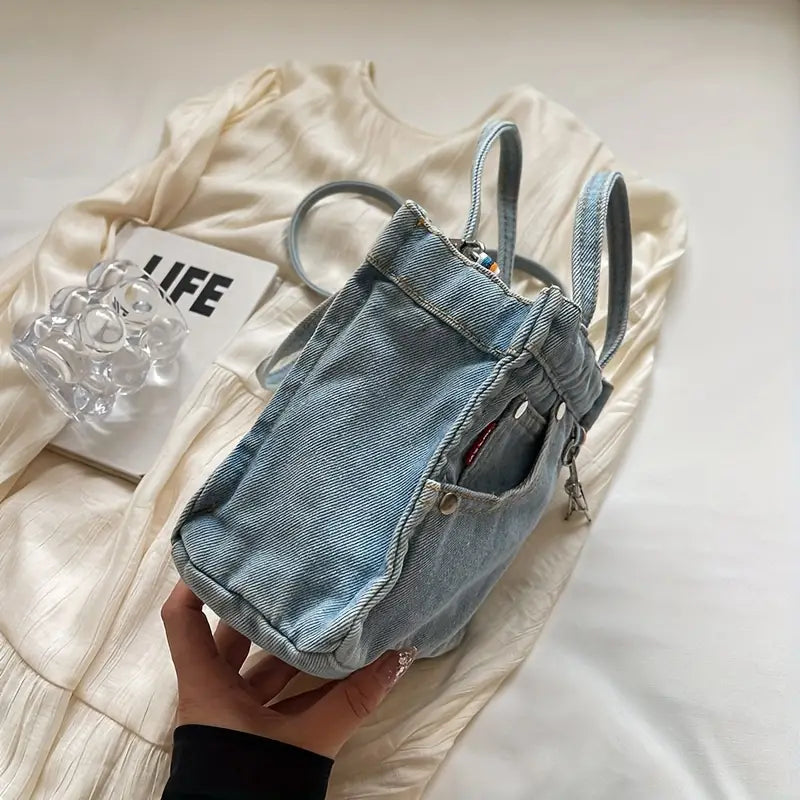 Zaino in denim chiaro su abito bianco, con accessori trasparenti. Design casual, perfetto per moda urbana e stile quotidiano.