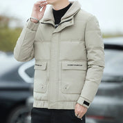 Giacca invernale uomo beige imbottita, colletto in pelliccia sintetica, tasche frontali, chiusura zip e bottoni, stile casual elegante.