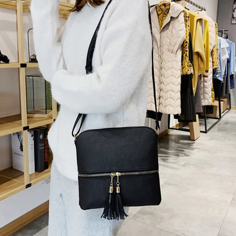 Borsa a tracolla nera in pelle con cerniera e nappine, indossata da una donna in negozio di abbigliamento. Elegante e versatile per ogni occasione.
