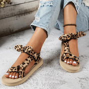 Sandali donna leopardati con fiocco, suola piatta beige, indossati con jeans strappati. Scarpe estive moda, stile casual chic.