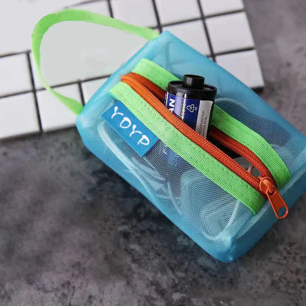 Custodia trasparente blu con cerniera arancione e verde, contenente una batteria. Design compatto, ideale per organizzare piccoli accessori.