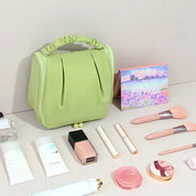 Borsa cosmetica verde con manico, circondata da trucchi: pennelli, rossetti, crema, profumo. Set trucco elegante e organizzato per viaggi.