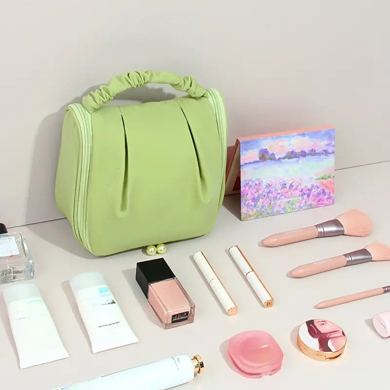 Borsa cosmetica verde con manico, circondata da trucchi: pennelli, rossetti, crema, profumo. Set trucco elegante e organizzato per viaggi.