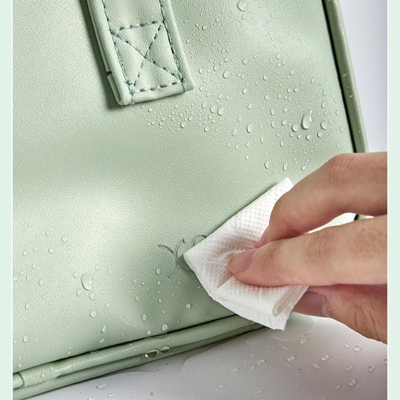 Mano pulisce borsa verde impermeabile con panno bianco, dettagli cuciture visibili. Accessorio moda resistente all'acqua, elegante e pratico.