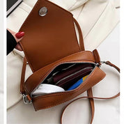 Borsa a tracolla in pelle marrone aperta, con cerniera, contenente portafoglio e oggetti personali. Design elegante e compatto per moda femminile.