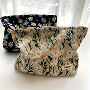 Due borse in tessuto con motivo floreale di margherite, una beige e una nera, su sfondo bianco. Ideali per organizzare accessori o cosmetici.
