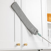 Spolverino in microfibra grigio su armadio bianco, manico estensibile, ideale per pulizia casa, rimozione polvere, accessori pulizia domestica.