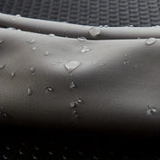 Tessuto impermeabile grigio con gocce d'acqua, texture liscia, ideale per abbigliamento outdoor e sportivo. Resistente e idrorepellente.