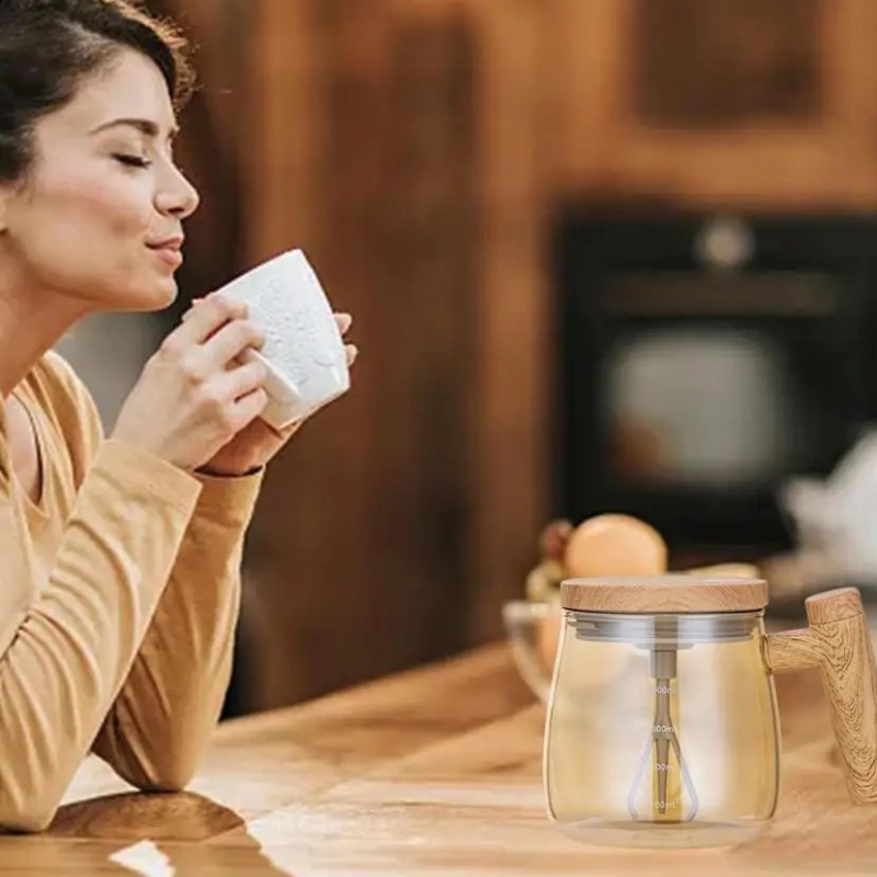 Donna che beve tè accanto a tazza di vetro con coperchio in legno su tavolo di legno. Design moderno, accessori cucina eleganti, ambiente accogliente.