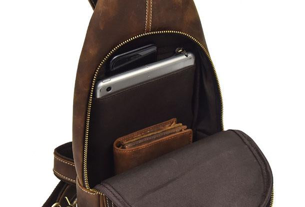 Zaino in pelle marrone con tasca aperta, contenente tablet, smartphone e portafoglio. Design elegante e funzionale, ideale per viaggi e lavoro.
