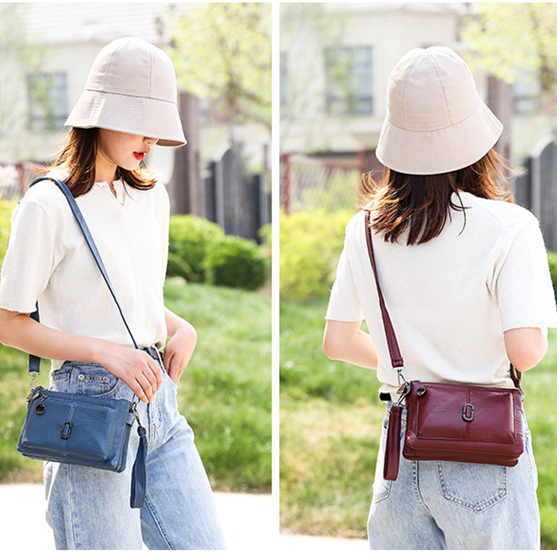Donna con cappello beige indossa borsa a tracolla in pelle blu e bordeaux, maglietta bianca e jeans. Moda estiva casual, accessori eleganti.