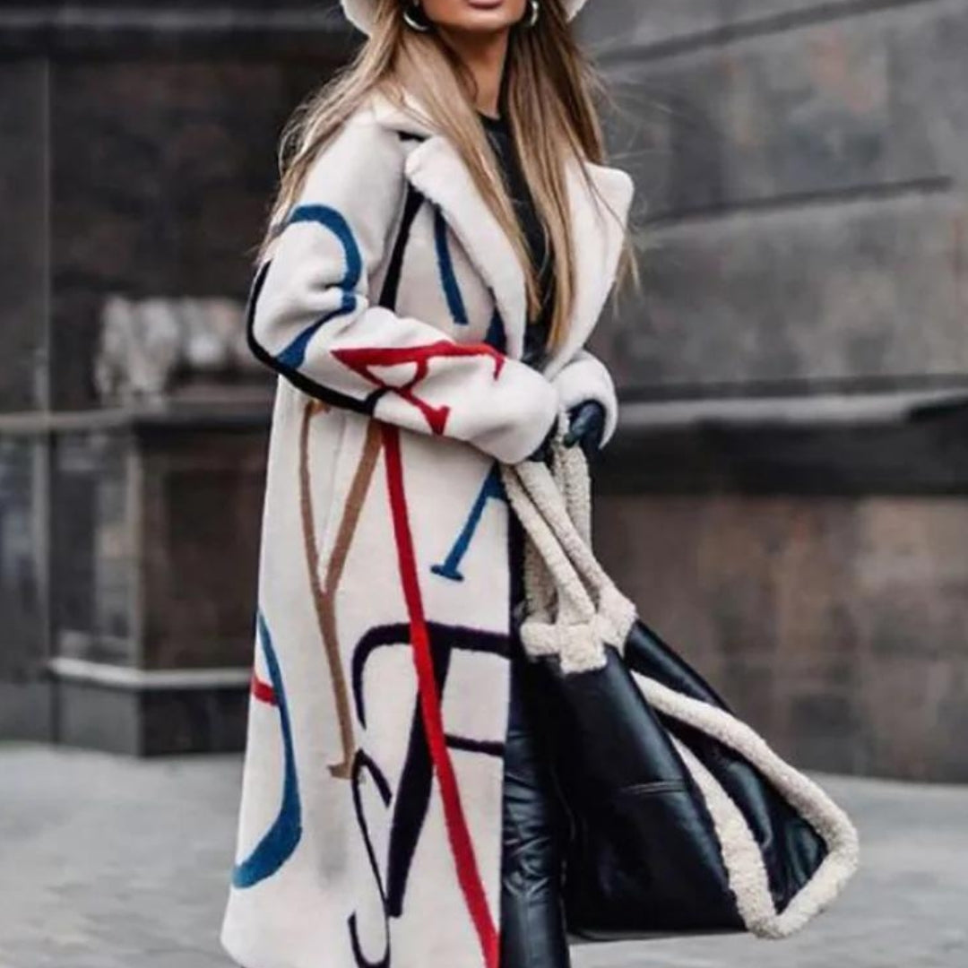 Cappotto invernale bianco con motivi geometrici colorati, indossato da donna con borsa nera in pelle e manici intrecciati. Moda autunno inverno.