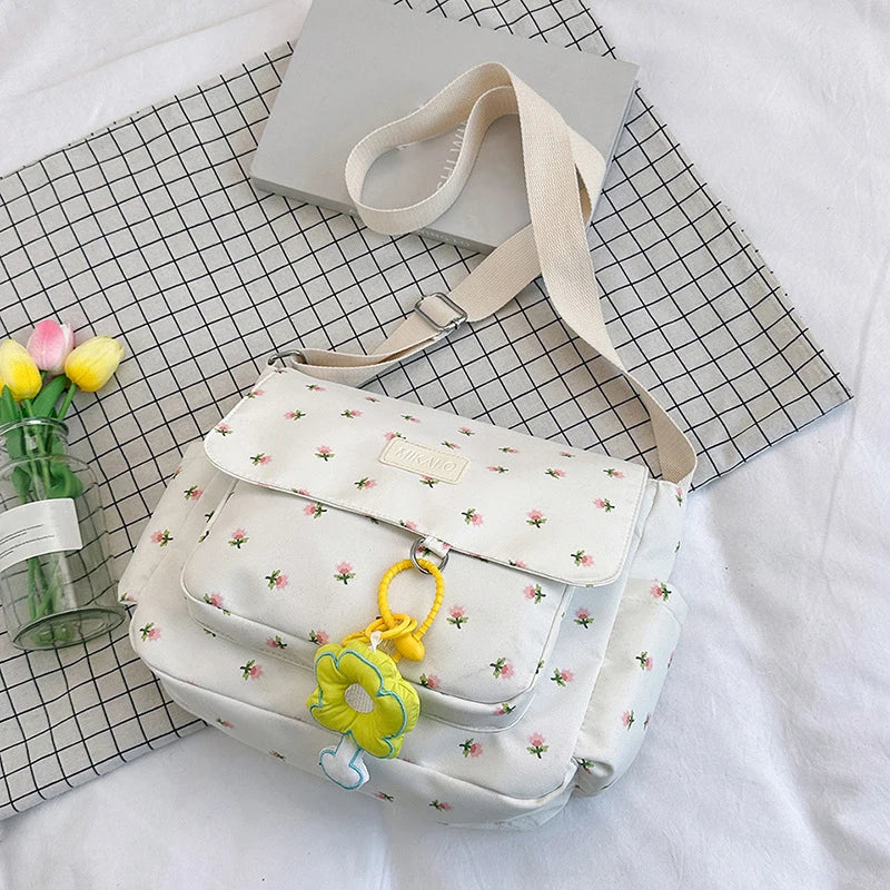 Borsa a tracolla bianca con stampa floreale, decorata con ciondolo a forma di fiore, su sfondo a quadretti. Accessorio moda donna elegante.