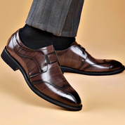 Scarpe eleganti uomo in pelle marrone lucida, design classico, indossate con pantaloni grigi. Scarpe formali di alta qualità per occasioni speciali.