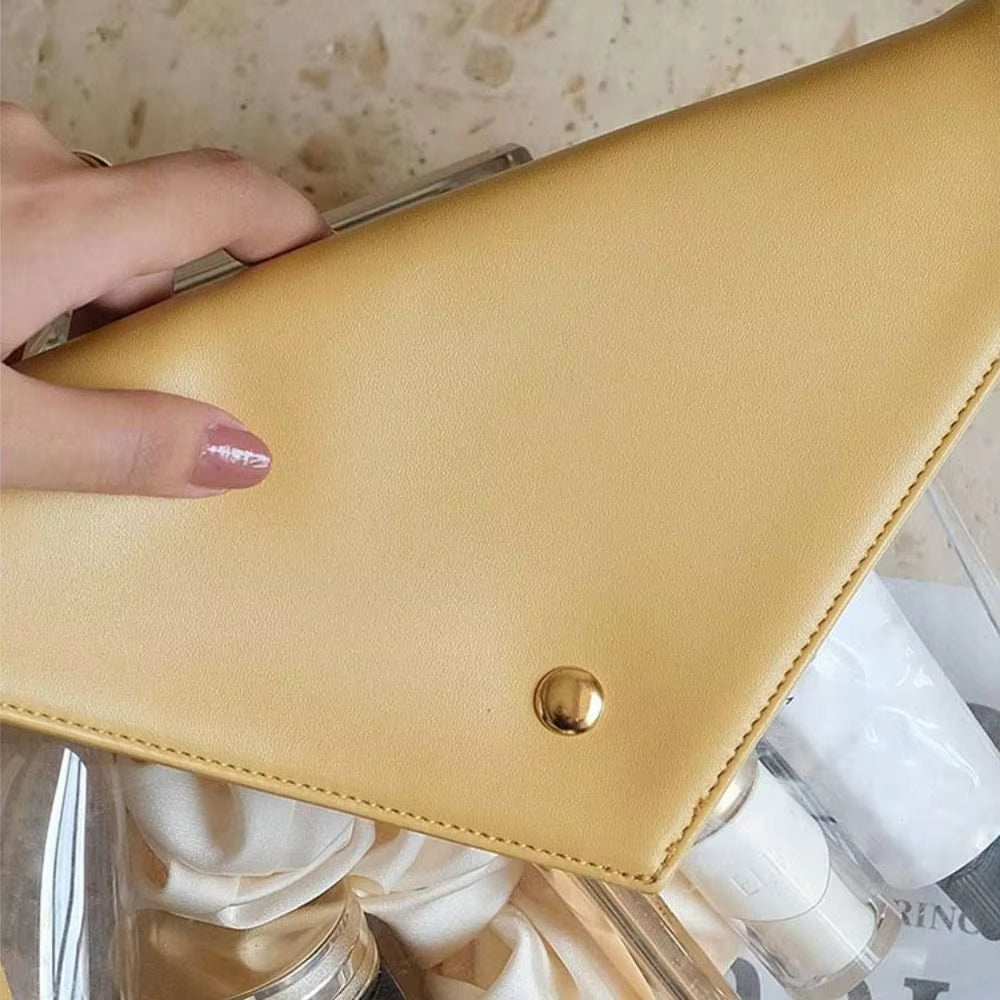 Utente che tiene una borsa a mano gialla in pelle sintetica con chiusura a bottone dorato, su sfondo di marmo. Accessorio moda elegante e moderno.