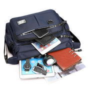 Zaino blu multifunzione con tasche aperte, contenente tablet, smartphone, orologio, portafoglio, chiavi auto e quaderno. Accessori viaggio uomo.