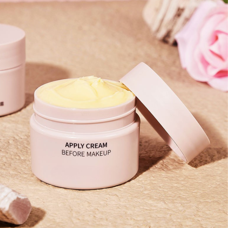 Crema viso idratante in barattolo rosa aperto, texture morbida, ideale come base trucco. Sfondo con rosa e asciugamano. Skincare quotidiana.