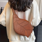 Borsa a tracolla in pelle marrone a forma di foglia, indossata su una felpa bianca. Design unico, moda autunno, accessorio elegante.