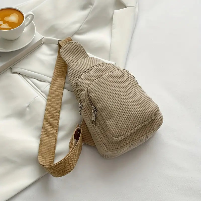 Zaino a tracolla beige in tessuto a coste su sfondo bianco, con tazza di caffè. Design casual, ideale per moda urbana e viaggi.