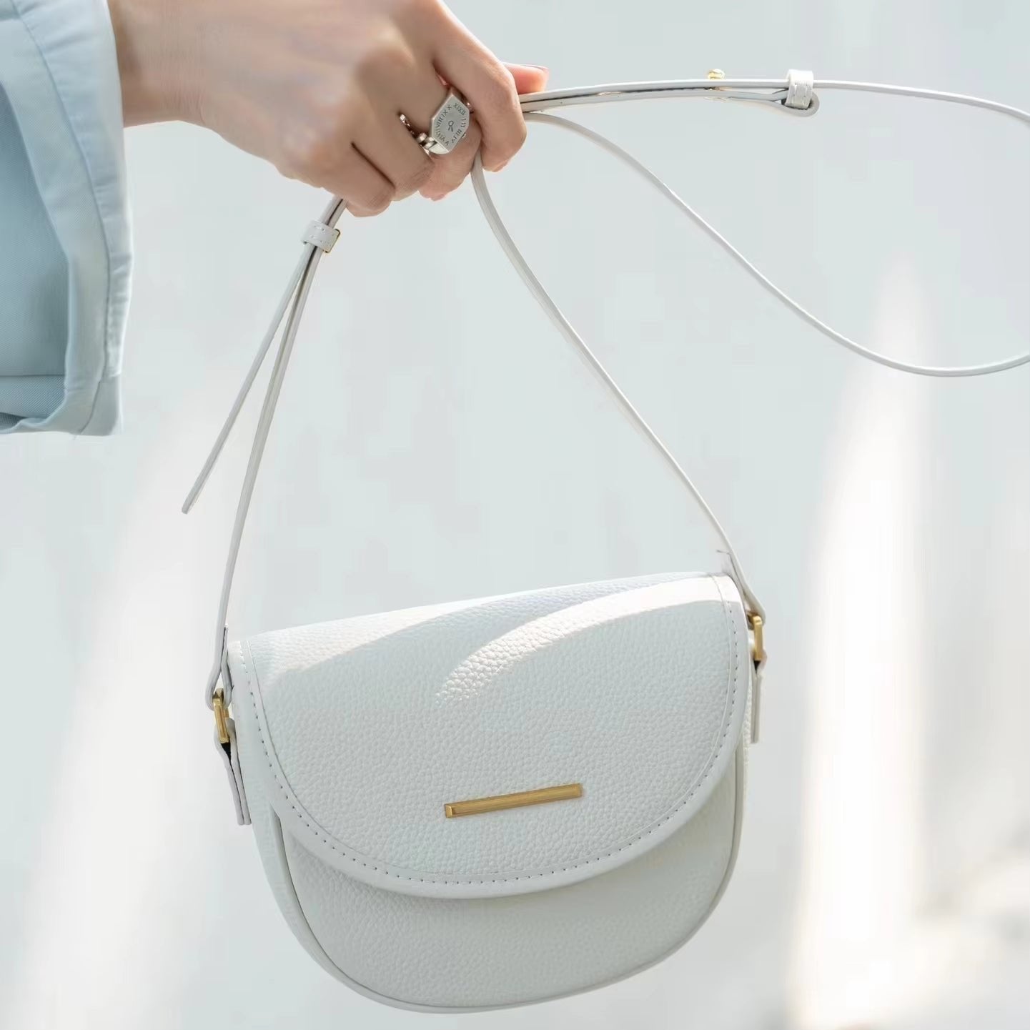 Borsa a tracolla bianca in pelle, design elegante e minimalista, chiusura con patta, dettagli dorati, ideale per moda femminile e accessori di lusso.
