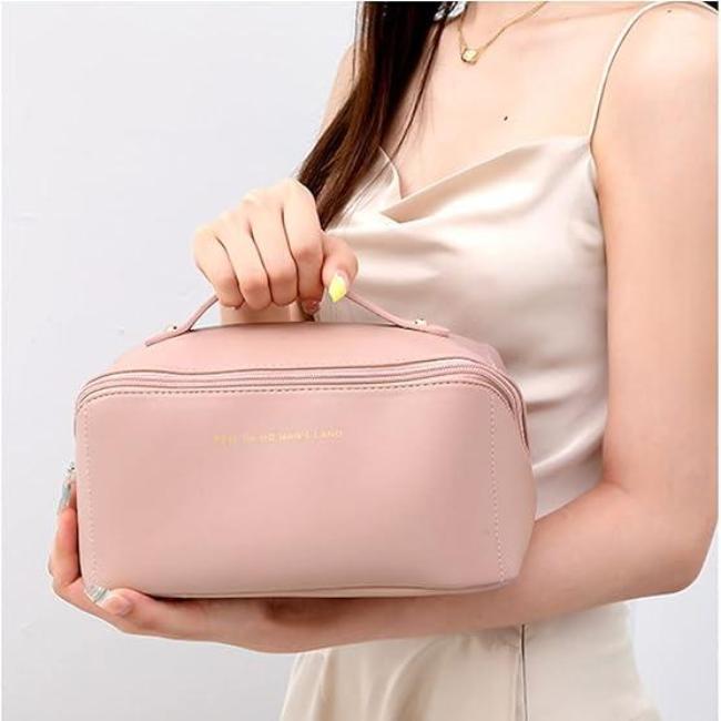 Borsa cosmetica rosa tenue, elegante e compatta, con cerniera dorata, tenuta da una donna in abito chiaro. Accessorio moda femminile.