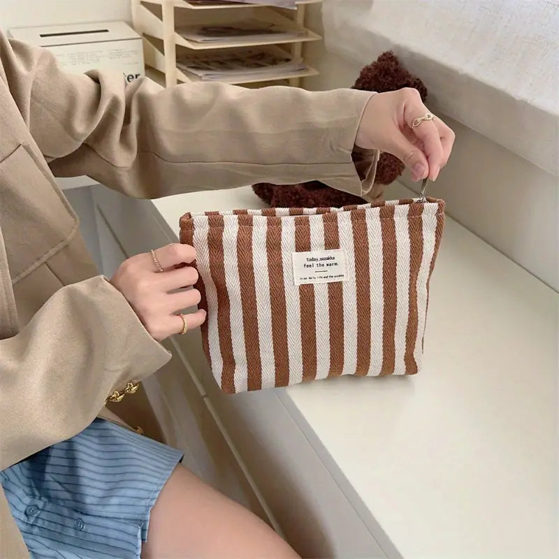 Borsa a righe marroni e bianche in tessuto, chiusura a zip, tenuta da una persona. Accessorio moda casual, ideale per organizzare piccoli oggetti.
