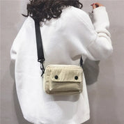 Donna con maglione bianco indossa borsa a tracolla beige in velluto a coste, design casual, moda autunno inverno, accessorio femminile trendy.