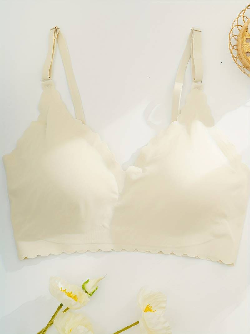 Reggiseno senza cuciture color crema con spalline regolabili, design a bordo smerlato, su sfondo bianco con fiori decorativi.