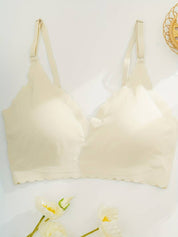 Reggiseno senza cuciture color crema con spalline regolabili, design a bordo smerlato, su sfondo bianco con fiori decorativi.