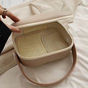 Borsa termica beige aperta su letto, design elegante, ideale per picnic e viaggi. Interno isolante, manico in pelle, perfetta per conservare cibi freschi.