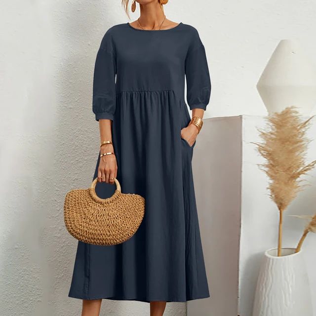 Donna con abito lungo blu scuro, maniche a tre quarti, borsa in paglia, sfondo minimalista. Moda elegante, abbigliamento femminile casual.
