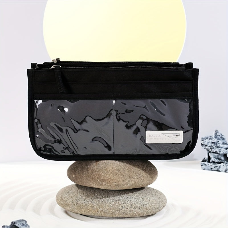 Borsa a tracolla nera con tasche trasparenti, posizionata su pietre impilate. Design moderno, ideale per moda urbana e viaggi.