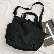 Zaino nero multifunzione su letto bianco, design elegante con tasche laterali e manici regolabili. Accessorio moda versatile e pratico.