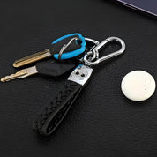 Portachiavi in pelle intrecciata nera con moschettone, due chiavi e un portachiavi blu su sfondo nero. Accessorio elegante e funzionale.