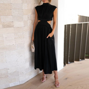 Abito lungo nero elegante con cut-out laterali, indossato da donna in sandali con tacco, borsa chiara. Perfetto per eventi serali e moda estiva.