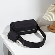 Marsupio nero elegante su tavolo bianco, con cerniera argentata e tasca aggiuntiva. Accessorio moda unisex, ideale per viaggi e uso quotidiano.
