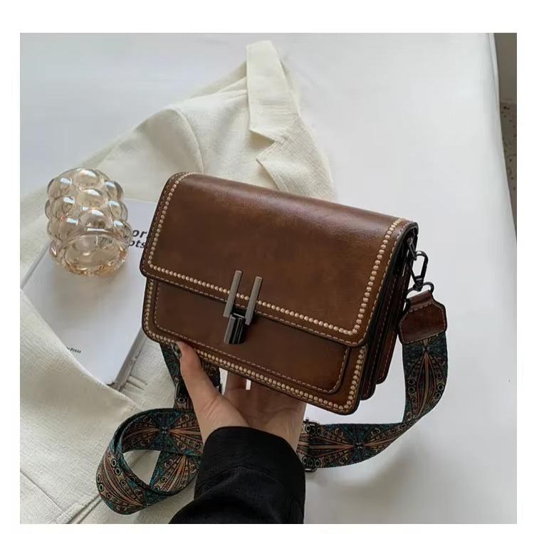 Borsa a tracolla in pelle marrone con fibbia metallica, dettagli cuciti, e tracolla decorata. Elegante accessorio moda per donna.