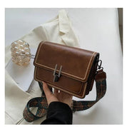 Borsa a tracolla in pelle marrone con fibbia metallica, dettagli cuciti, e tracolla decorata. Elegante accessorio moda per donna.
