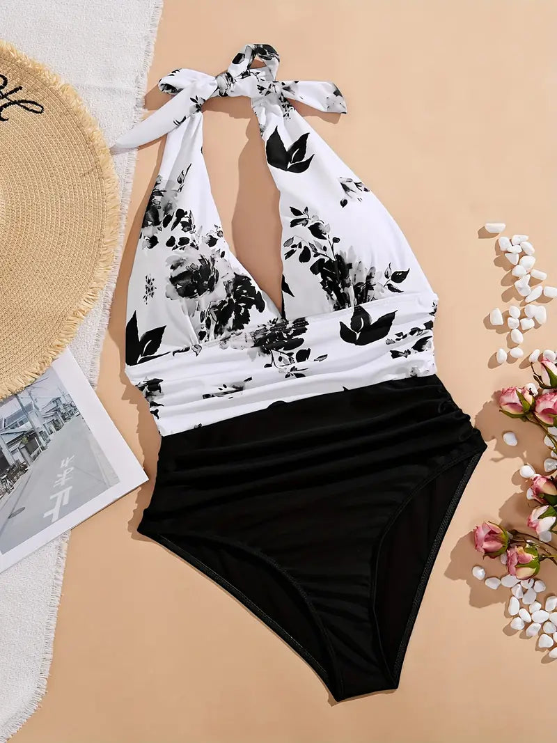 Costume intero donna bianco e nero con stampa floreale, scollo all'americana. Accessori: cappello di paglia, fiori rosa, ciottoli bianchi.