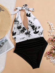 Costume intero donna bianco e nero con stampa floreale, scollo all'americana. Accessori: cappello di paglia, fiori rosa, ciottoli bianchi.